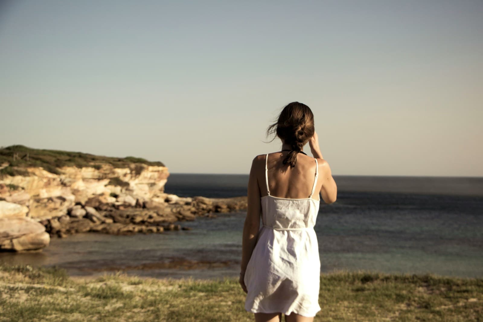 A woman walking through coastal grass above the sea